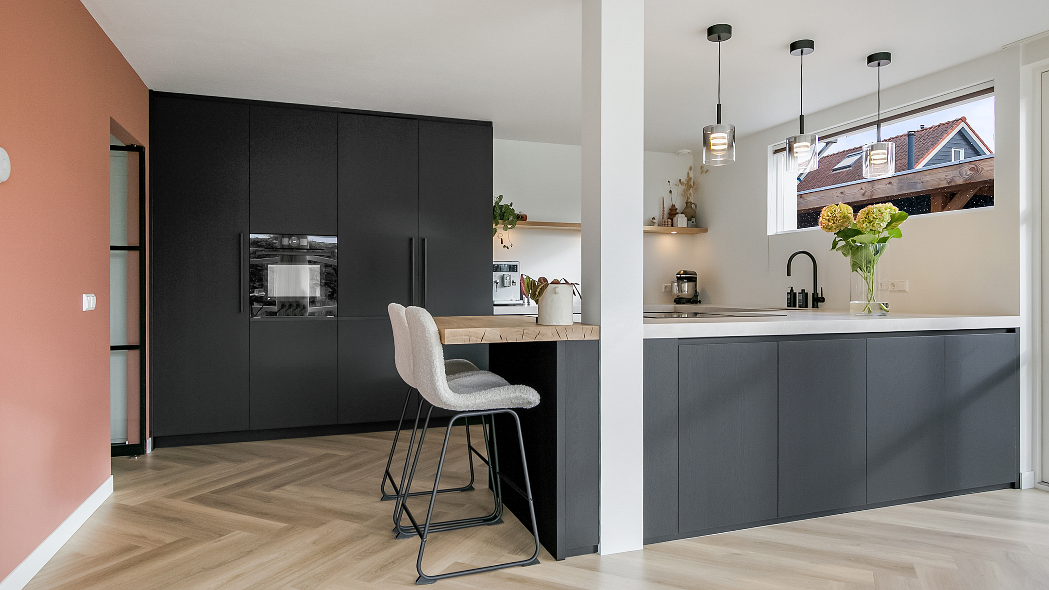 Donkere keuken met licht keukenblad en beige stoelen.